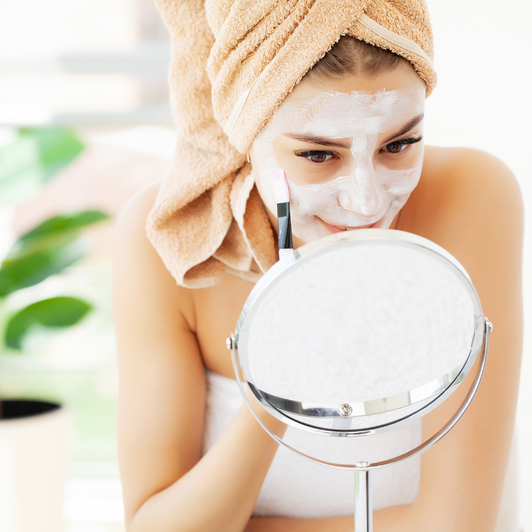 white woman applying face mask with brush, looking in mirror
